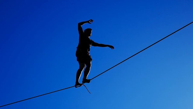 Silhouette of a man walking on a tightrope against the sky. Rope-walker.