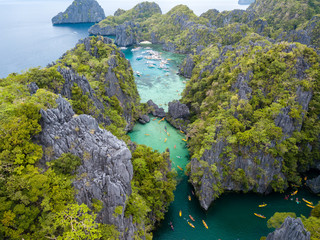 Aerial drone view of kayaks and boats around a beautiful tropical lagoon surrounded by vertical limestone cliffs