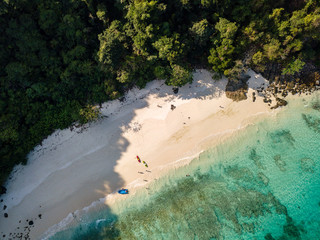 Aerial drone view of people on a small tropical beach surrounded by jungle and coral reef