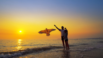 Father And Son Flying Kite on Sea Coast with nice Orange Sky Sunset. Steadicam Shot