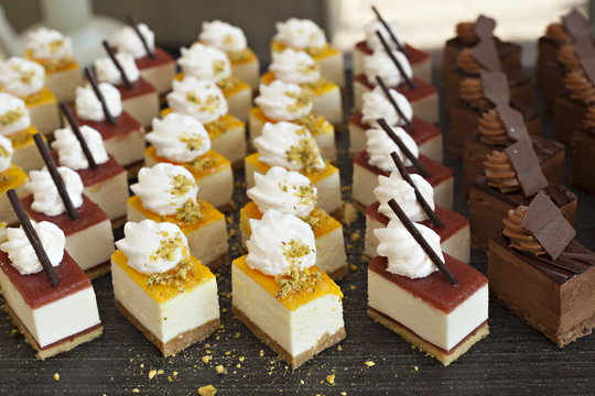 Small assorted cakes lined up in rows on dessert buffet