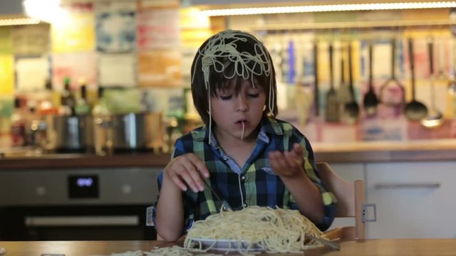Little preschool boy, cute child, eating spaghetti for lunch and making a messat home in kitchen