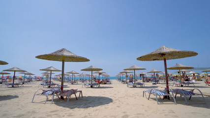Summer beach resort bar lounge area with wooden easy chairs and straw parasols lined up next to the sea water