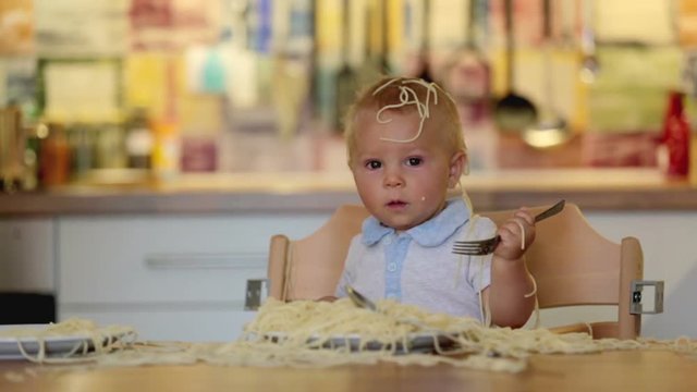 Little baby boy, toddler child, eating spaghetti for lunch and making a mess at home in kitchen