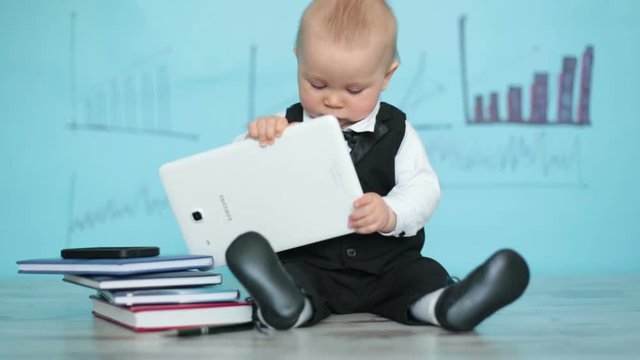 Cute toddler boy, dressed in suit and bow, talking on the phone and playing on tablet, writing in diary