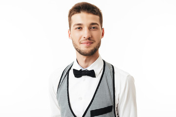 Portrait of young smiling waiter with beard in bow tie dreamily looking in camera over white background isolated
