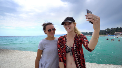 Funny female friends on vacation taking selfies on the beach with a smart phone