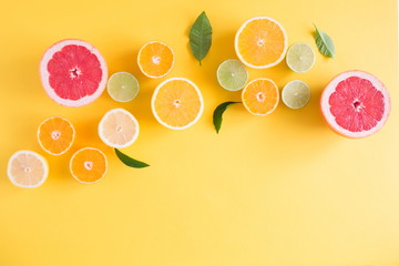 Creative background made of summer tropical fruits with leaves, grapefruit, orange, tangerine, lemon, lime on pastel yellow background. Food concept. Flat lay, top view, copy space 