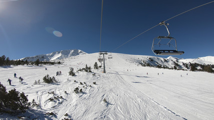 Fototapeta na wymiar Ski lift draging through a pine forest area at sunrise to the mountain ski slopes winter resort, POV shot