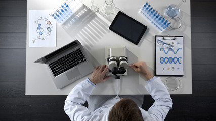 Scientist working on computer and microscope in laboratory, research top view