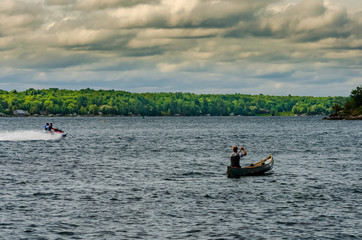 Fototapeta premium Man canoeing next to a watercraft on the St. Lawrence River under a cloudy sky