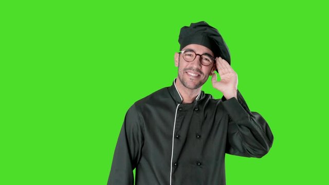 Naughty young chef trying to listen something with his hand against green background