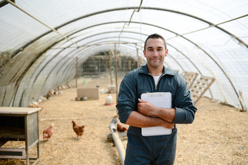 portrait of handsome young farmer veterinarian taking care of poultry in a small chicken farm