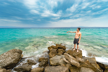 Lonely lost man standing in front of the pacific ocean and hand pointing to sea horizon