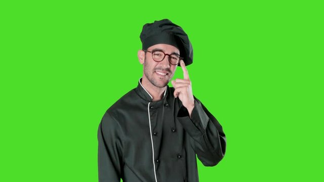 Confident young chef doing a gesture of observe with his finger against green background