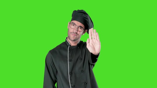 Serious young chef with a gesture of stop showing his palm against green background