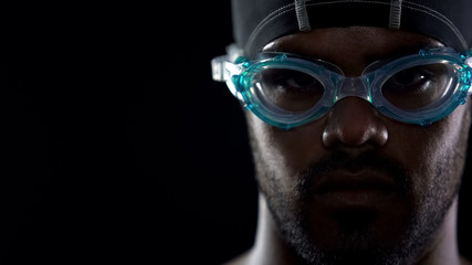 Closeup of concentrated male swimmer face in goggles, looking directly at camera