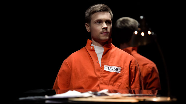 Handcuffed maniac in orange prison jumpsuit looking around in interrogation  room Stock Photo | Adobe Stock