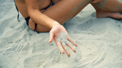 Sexy woman sitting on beach with sand running through fingers