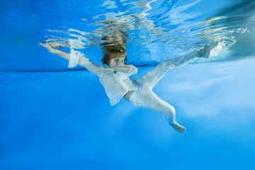Boy in a white shirt and trousers poses underwater