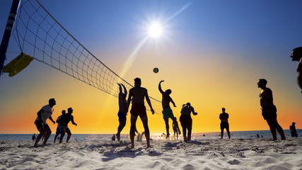 Unrecognizable people play Volleyball on the beach, at Sunset