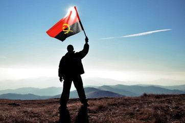 Successful silhouette man winner waving Angola flag on top of the mountain peak - obrazy, fototapety, plakaty