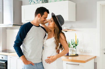 Beautiful young modern couple expecting a baby, looking with love at eachother in their home kitchen.