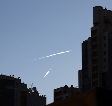Two aircraft with traces in the sky against the background of modern buildings