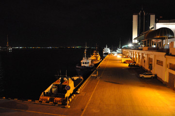 Berth in the port. Small tugboats and pleasure boats are moored to the left. Wide road, convenient access by car. Night shooting. View from above. 