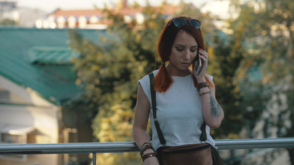 Young redhaired woman riding bicycle in city. Woman with mobile phone