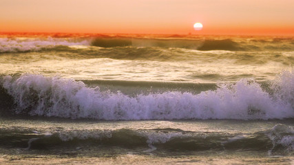 Panele Szklane Podświetlane  Fale burzowe wylewają się na plażę, gdy słońce zachodzi o zachodzie słońca, Zwolnione tempo
