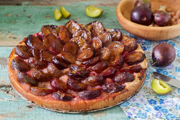 Sweet pie from short pastry with caramelized plums and ripe plums on a wooden table. Rustic style.