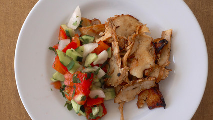 Pieces of chicken meat in breadcrumbs and fresh vegetables. The chicken on the plate rotates against the background of the wooden table. Top view, close-up.