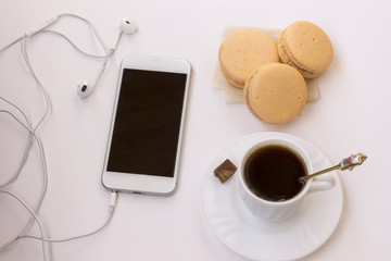Business concept: phone with headphones, a cup of coffee and a cake on the table. Close-up. Top view.