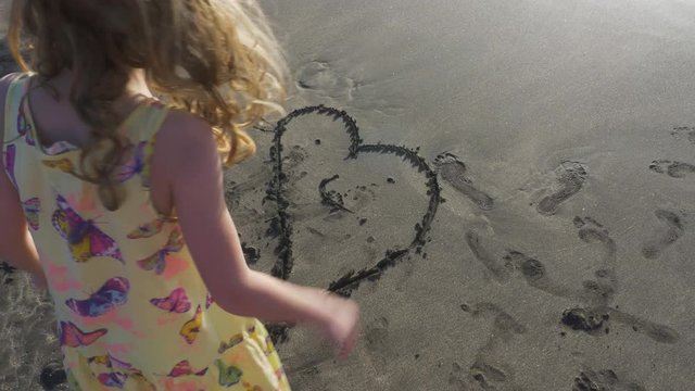 Child Tracing Heart Shape and Smile in Beach Sand