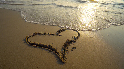 Summer romantic vacation concept of hearth on sand being washed by sea waves at sunset