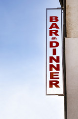 Neon lit BAR DINNER sign in daylight