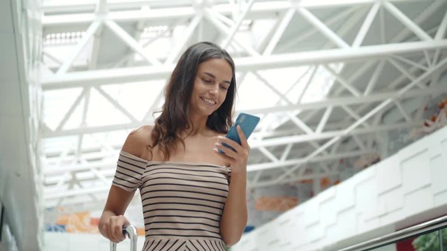 Happy young woman using smart phone in shopping mall. Business woman freelancer with smartphone in airport terminal walking tourist.