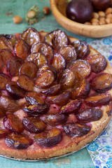 Sweet pie from short pastry with caramelized plums and ripe plums on a wooden table. Rustic style.