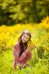 Naklejka na ściany i meble Smiling girl sitting in the field of spring yellow flowers