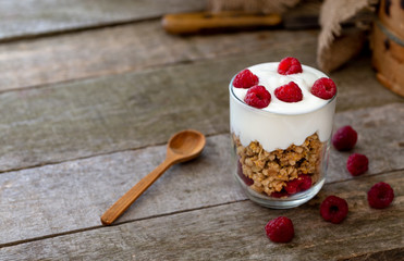 Yogurt with muesli in glass bowl with pieces raspberries on top.