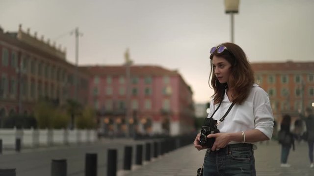 Beautiful woman photographer in white shirt with long dark hair making shots of Nice, France with old school camera. A tram. Cloudy spring day. Right to left pan slow motion medium shot