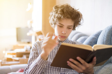 young smiling teenager lying on the sofa and reading a book at home