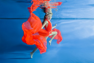   girl in long, bright dresses wearing poses underwater 