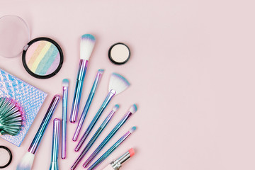 Fashion holographic colored makeup brushes with eye shadow, powder and other cosmetic products   on a pastel pink background. Flat lay, top view