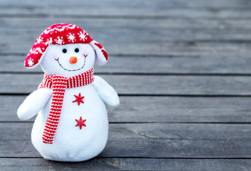 cheerful and funny snowman in a red hat and red scarf on a gray wooden background