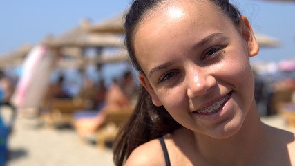 Beautiful happy teen girl with tooth braces smiling to camera sitting on beach during summer vacation