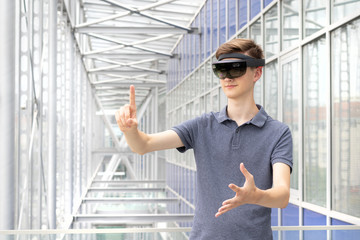 Portrait of young Caucasian teenager using augmented reality HoloLens in modern building. Goggles controlled by various gestures and air taps.