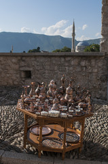Bosnia Erzegovina: un tavolino con set di rame di tè e caffè in vendita e vista sullo skyline di Mostar con la moschea Koshi Mehmed Pasha sullo sfondo