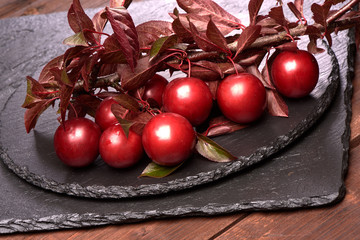 Red cherry plums fruits with leaves on a slate stone plate on a wooden rustic background.